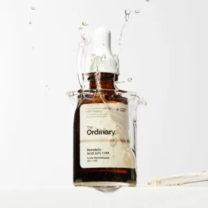 بطری شیشه‌ای قهوه‌ای سرم لایه بردار مندلیک اسید ۱۰% + هیالورونیک اسید The Ordinary در حال فرو رفتن در آب و تشکیل حباب